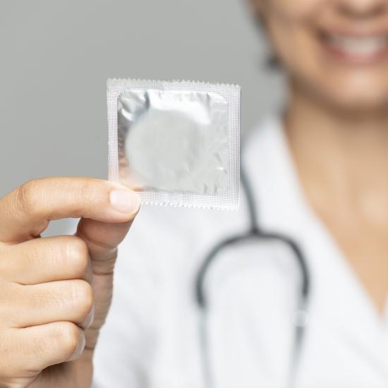 A smiling doctor holds a condom in a silver wrapper, signifying access to birth control.